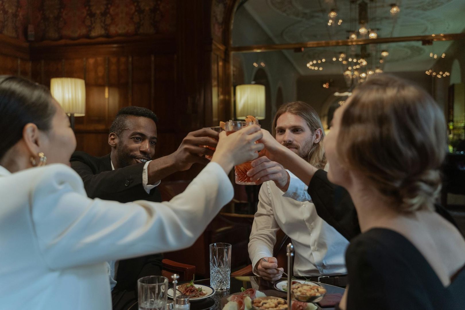 En grupp vänner skålar med drinkar på en elegant abonnerad restaurang.