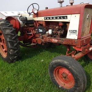 En röd begagnad Farmall 504 traktor på en gräsmatta framför en lada.