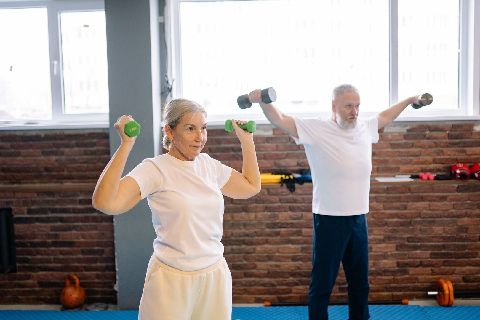 Två äldre vuxna styrketränar med hantlar i ett gym
